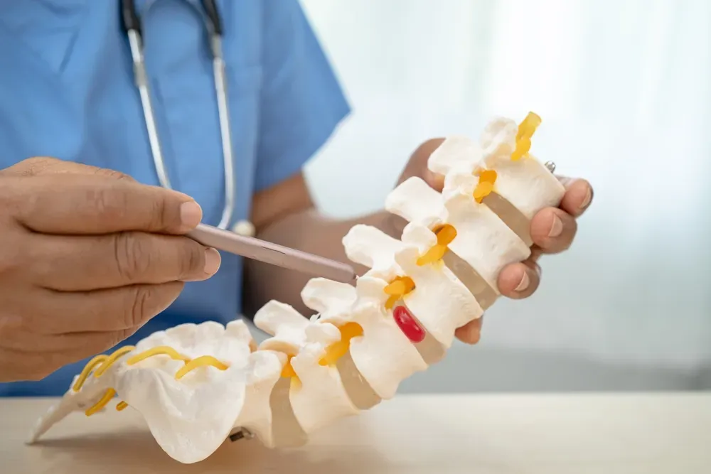 A doctor in blue scrubs points to a spinal model, highlighting a disc issue — illustrating degenerative disc disease treatment options available in Morganville, NJ.