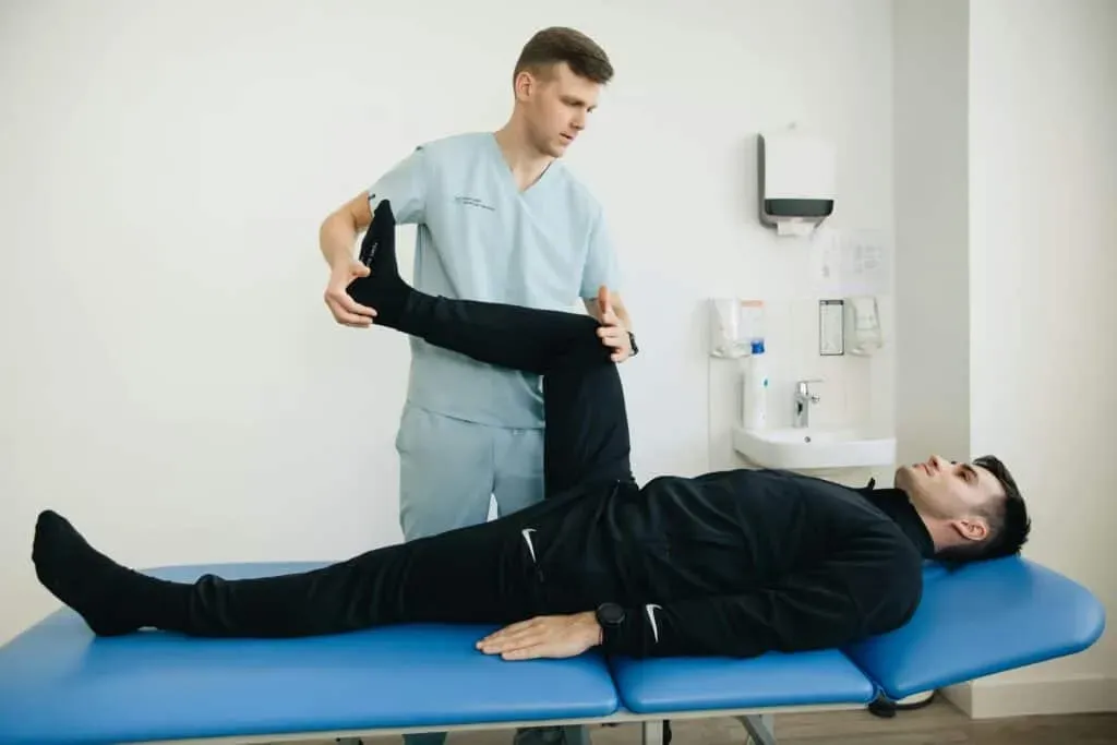 Limitless Healthcare Team performs physical therapy on a patient lying on a blue medical table, stretching the patient's leg toward their chest.