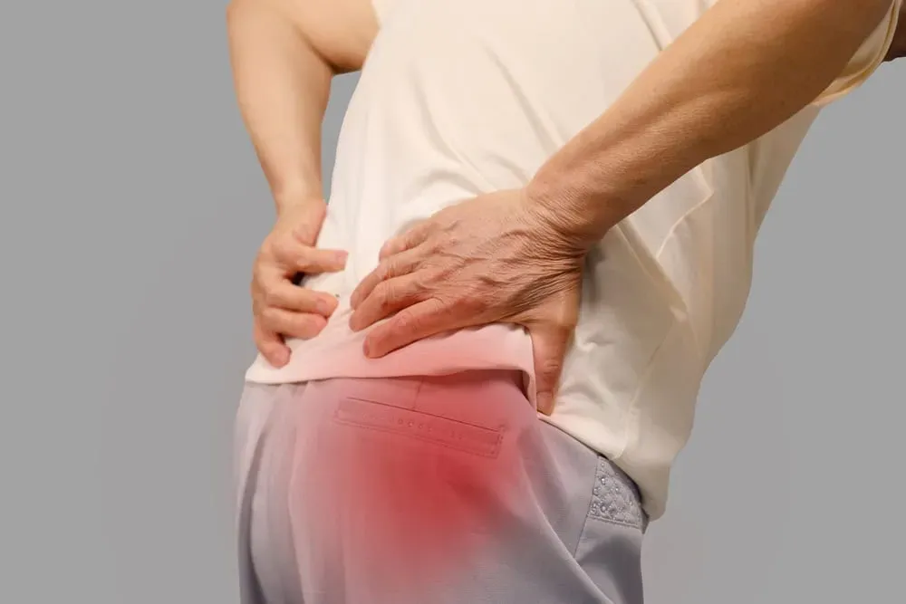 A person in a white shirt clutches their lower back and hip, with a red overlay indicating areas of back pain. Limitless Spine & Joint Care offers integrated care in Morganville, NJ.